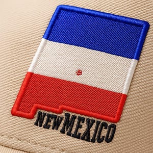Pode incluir: Boné de beisebol bege com um patch bordado da bandeira do estado do Novo México. O patch tem seções azuis, brancas e vermelhas, e o texto "NEW MEXICO" é costurado em preto.
