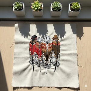 May include: Embroidered fabric square depicting four figures with long braids and colourful shawls, standing on stylized feather designs. The figures are in shades of red, brown, and white. The fabric is a natural off-white colour.