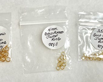 May include: Three clear plastic bags containing gold-plated jump rings. The bags are labelled with sizes and quantities: 5mm, 4mm, and 3.5mm. The labels also indicate the weight of the rings.