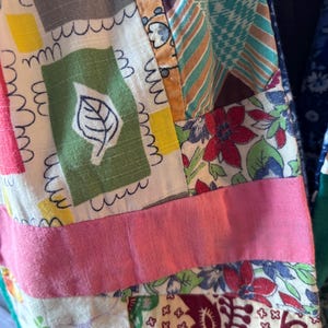 Puede incluir: Primer plano de un textil patchwork con una variedad de telas estampadas. El diseño incluye cuadrados con motivos de hojas y flores, rayas y una cinta rosa. Los colores incluyen verde, rosa, azul y marrón.