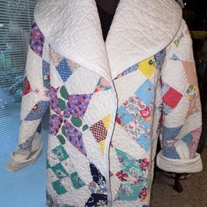 May include: A long-sleeved quilted coat featuring a patchwork design of various floral and geometric patterns in shades of blue, red, yellow, purple, and green, finished with a solid white wide collar and matching white cuffs.