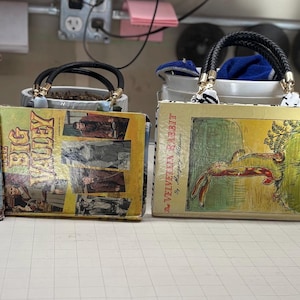 May include: Four vintage book purses with black braided handles and gold-tone hardware. The purses feature book covers with titles like "Lassie," "Big Valley," "The Velvet Rabbit," and "King Kong." Each purse has a unique design and color scheme.
