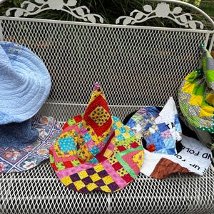 May include: Four quilted fabric hats with pointed crowns. One is light blue with floral patterns, one features a vibrant patchwork of red, yellow, pink, and blue squares, one is a blue and white floral print, and one is a green and yellow patchwork.