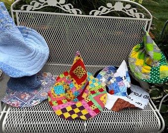 May include: Four quilted fabric hats with pointed crowns. One is light blue with floral patterns, one is a patchwork of bright red, yellow, pink, and blue squares, one is a blue and white patchwork, and one is a green and yellow patchwork.