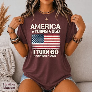 May include: A heather maroon t-shirt featuring white text that reads AMERICA TURNS 250 and I TURN 60, with the years 1776, 1966, and 2026 printed below. A distressed graphic of the American flag is centered between the two lines of text.