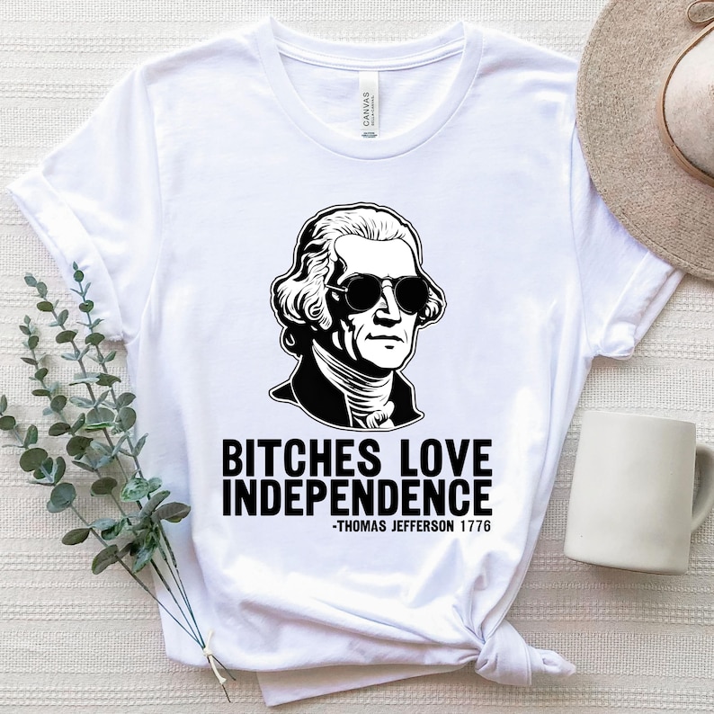May include: White t-shirt with a black and white illustration of Thomas Jefferson wearing sunglasses. The text "Bitches Love Independence -Thomas Jefferson 1776" is printed below the illustration.