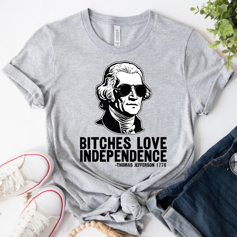 May include: Gray t-shirt with a black and white illustration of Thomas Jefferson wearing sunglasses. The text "Bitches Love Independence -Thomas Jefferson 1776" is printed below the illustration.