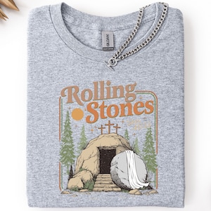 May include: Grey t-shirt featuring a vintage-style graphic of a tomb with a rolling stone and the text "Rolling Stones".