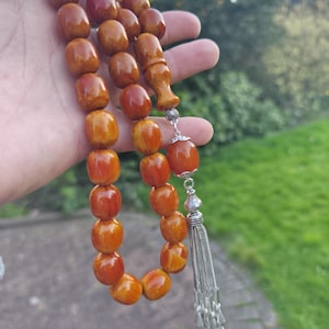 May include: A brown amber prayer beads necklace with a silver tassel. The beads are round and have a natural, organic look.