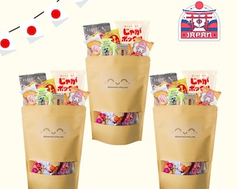 May include: Three tan stand-up pouches filled with assorted Japanese snacks. Each pouch features a clear window at the bottom, a smiling face graphic, and the text DLSnacksCoEtsy.com. The top of each pouch displays various colorful snack packages.