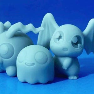 May include: Three light blue figurines of fantasy creatures. One has large ears and a horn, another is round with a smiling face, and the third has large eyes and wings. The figurines are on a blue surface.