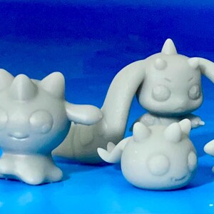 以下が含まれることがあります： 丸みを帯びた体と尖った突起のある3つの灰色のフィギュア。1つは腕を広げ、もう1つは長く湾曲した腕を持ち、3つ目は小さくて丸いです。フィギュアは青い背景に配置されています。