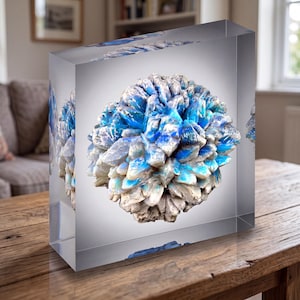 May include: A clear rectangular acrylic block containing a spherical cluster of white and vibrant blue crystalline structures. The object features a multi-faceted, textured surface with deep blue hues transitioning into opaque white tones.
