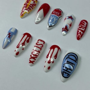 May include: A collection of ten long, almond-shaped artificial nails. Designs include red and white patterns, text, and graphic elements. Some nails feature dripping blood designs, while others display text like "Miss" and "EST19XX".