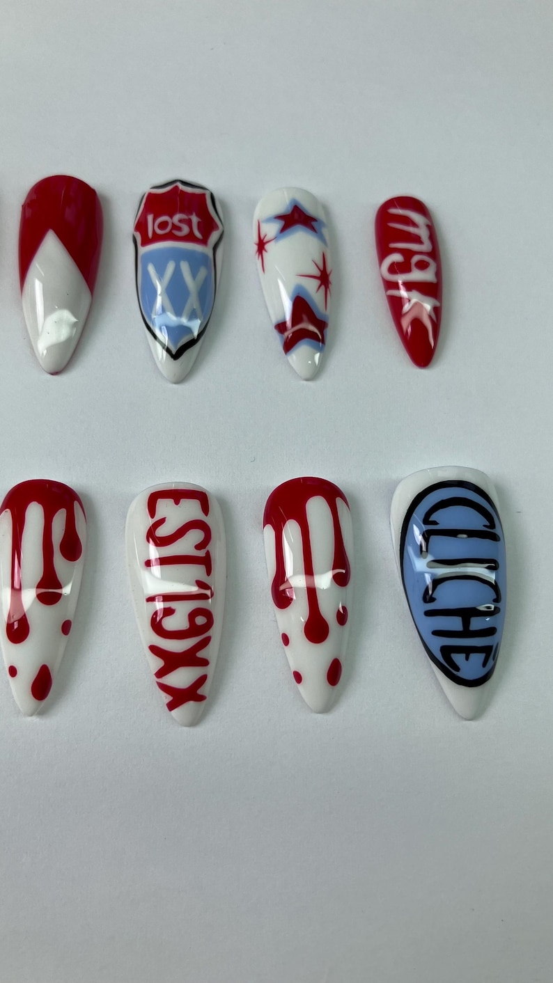 May include: A set of ten long, almond-shaped artificial nails. Designs include red and white geometric patterns, text that reads "lost", "EST 19XX", "mgk", and "cliche", and red blood drop patterns on a white base.