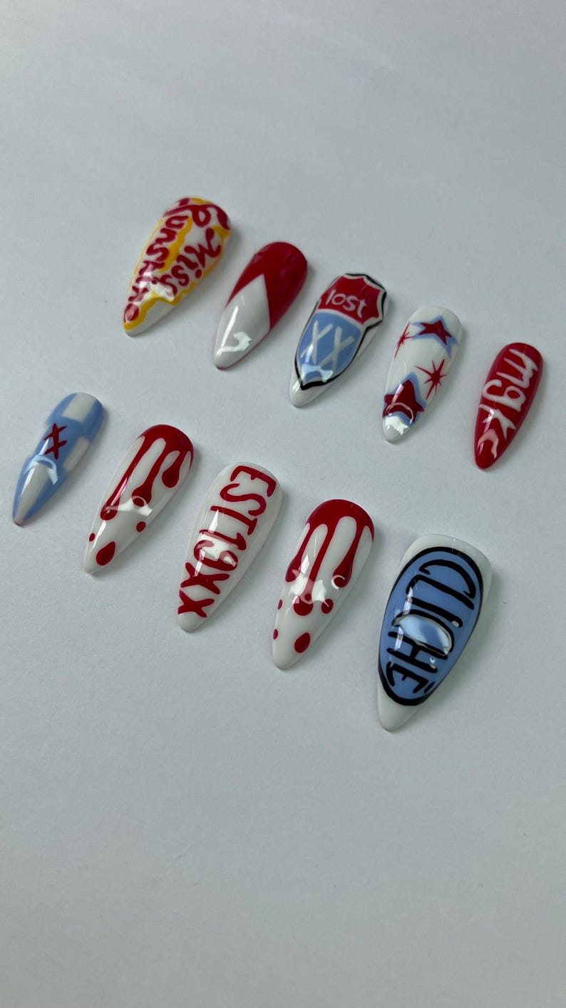 May include: A set of eleven artificial fingernails with various designs. The nails feature white, red, blue, and black colors, with text and graphic elements. Designs include dripping blood, stars, and the word "lost."
