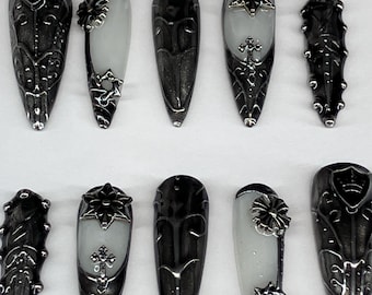 Puede incluir: Una selección de uñas de estilo gótico. Los diseños incluyen detalles metálicos ornamentados, decoraciones florales y una combinación de puntas de uñas sólidas y translúcidas. La paleta de colores es predominantemente plateada y negra.