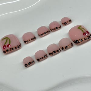 May include: Set of ten pink toe nails with a leopard print design and cherry accents.