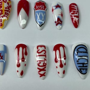 May include: A set of ten artificial fingernails with various designs. The nails feature white bases with red, blue, and black accents. Some nails have text, including "lost" and "EST19XX".