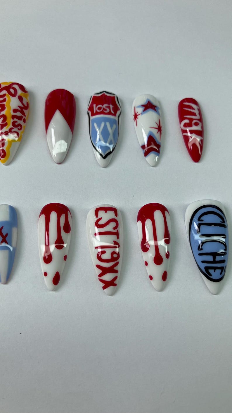 May include: A set of ten artificial fingernails with various designs. The nails feature white bases with red, blue, and black accents. Some nails have text, including "lost" and "EST19XX".