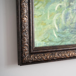 Pode incluir: Uma pintura a óleo emoldurada apresentando uma cena impressionista com pinceladas suaves em verde, azul e branco. A obra de arte está inserida numa moldura castanho-escura, ornamentada e em relevo com padrões de volutas nas bordas.