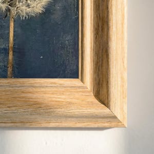 Könnte beinhalten: Gerahmtes Gemälde eines Löwenzahns vor dunklem blauem Hintergrund. Das Kunstwerk ist in einem hellbraunen Holzrahmen eingefasst. Der Fokus des Gemäldes liegt auf dem zarten, weißen Samenstand des Löwenzahns.