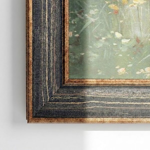 Puede incluir: Una obra de arte enmarcada con un marco de madera oscuro y texturizado. El marco tiene una apariencia desgastada y rústica con un borde interior dorado. La obra de arte dentro del marco representa un paisaje impresionista suave con verdes y amarillos apagados.