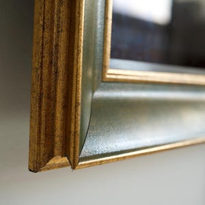 Pode incluir: Close-up de uma moldura decorativa com acabamento dourado e verde. A moldura tem um design detalhado e texturizado e uma borda chanfrada. A moldura é feita de madeira e tem um estilo clássico e elegante.