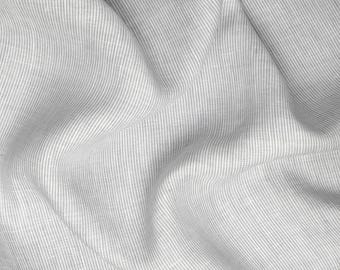 May include: Close-up of a textured, light gray fabric with vertical white stripes. The fabric is draped, creating soft folds and shadows. The material appears to be linen or a similar woven textile, suitable for clothing or home decor.
