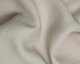 May include: Close-up of a soft, light beige linen fabric with a subtle texture. The fabric is folded and draped, showcasing its natural drape and wrinkles.