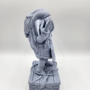 以下が含まれることがあります： 長いひげととがった帽子をかぶったファンタジーな生き物の3Dプリントフィギュアで、楽器を持っています。フィギュアはレンガの土台の上に木製のプラットフォームで立っています。