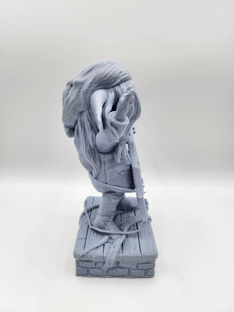 以下が含まれることがあります： 長いひげととがった帽子をかぶったファンタジーな生き物の3Dプリントフィギュアで、楽器を持っています。フィギュアはレンガの土台の上に木製のプラットフォームで立っています。