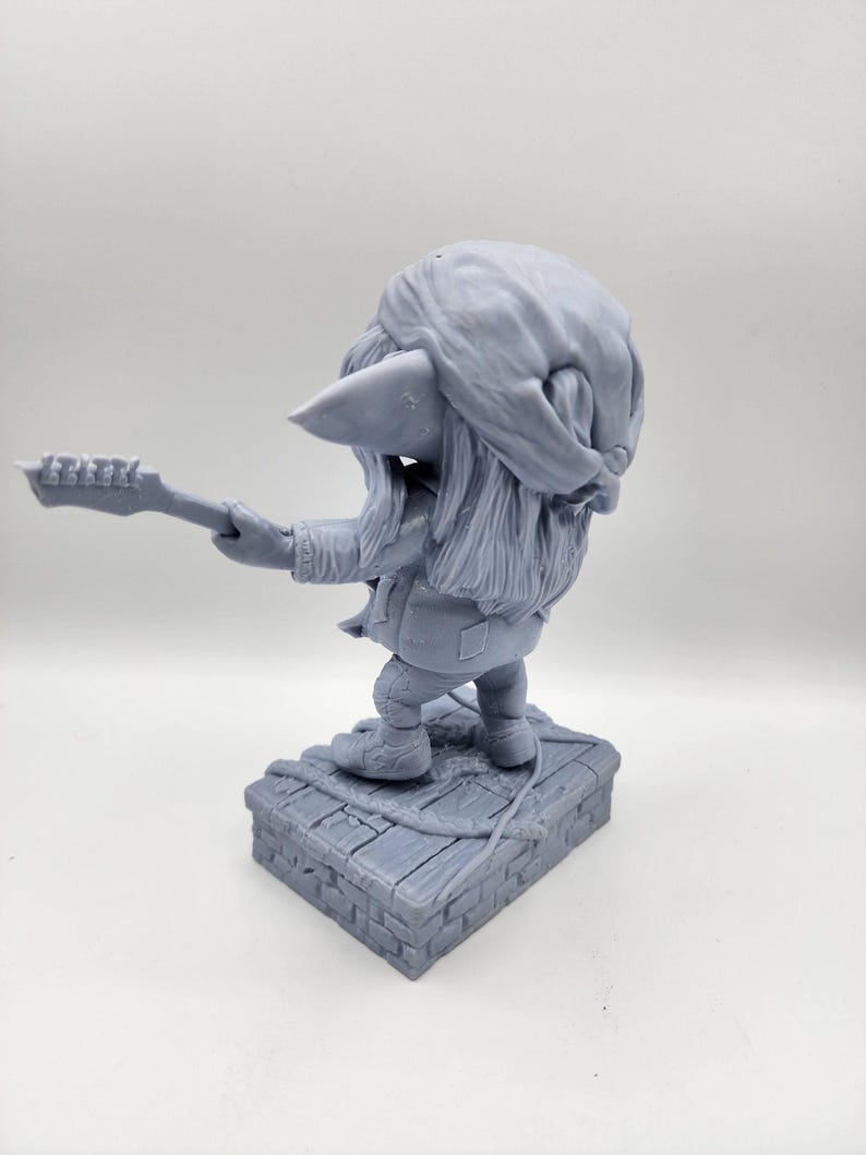 以下が含まれることがあります： ギターを弾いているゴブリンのグレーの3Dプリントフィギュア。ゴブリンはバンダナとジャケットを着ています。フィギュアはレンガの台座の上に立っています。