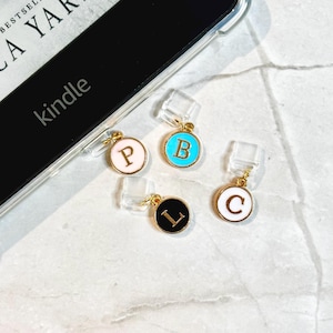 May include: Four gold-toned initial charms with clear attachments. Each charm features a different letter: P, B, L, and C. The letters are in black or white against a colored background, including pink, turquoise, and black. The word "kindle" is visible.