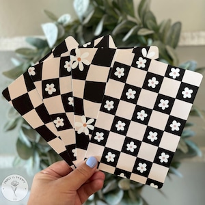 May include: Four black and white checkered patterned cards with white daisies on a pink background. The cards are held in a hand.