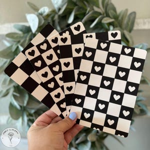 May include: Four black and white checkerboard patterned cards with white hearts on each square. The cards are held in a hand.