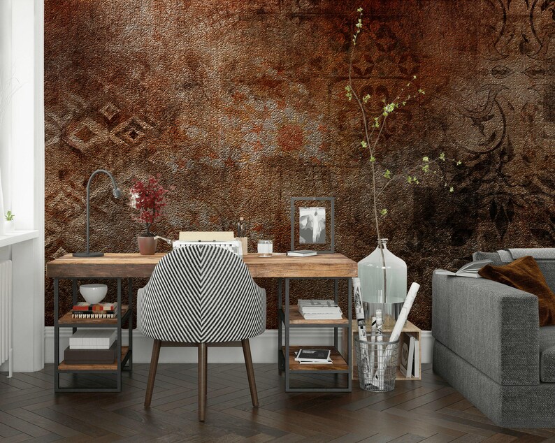May include: A home office setup featuring a wooden desk with a black and white striped chair. The desk has a metal frame and shelves, with a lamp, books, and decorative items. The background is a textured brown wall.