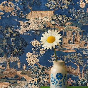Op de afbeelding: Een witte vaas met blauwe bloemmotieven houdt een madeliefje vast tegen een blauw-gouden landschapst behang. Het behang toont een Aziatisch geïnspireerde tuin met bomen, bruggen en pagodes. De vaas staat op een felgroen oppervlak.