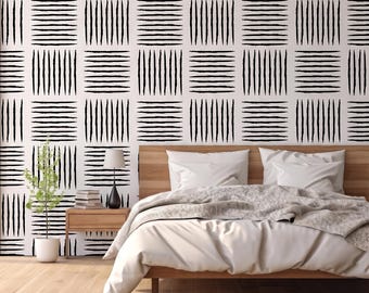 May include: A bedroom with a wooden bed frame, white bedding, and a patterned accent wall. The wall features a grid of white squares with black vertical and horizontal brushstrokes. A small plant and a lamp sit on a wooden nightstand.