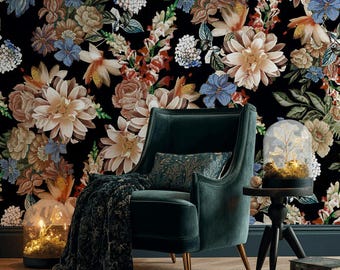 May include: A dark teal velvet armchair with gold legs, a patterned cushion, and a dark floral throw. The backdrop is a black floral wallpaper with large, colourful flowers. A small side table holds a glass cloche with fairy lights.