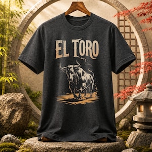Peut inclure: Un t-shirt &agrave; manches courtes gris anthracite fonc&eacute; avec une impression graphique repr&eacute;sentant un taureau en position de charge. Au-dessus du taureau, le texte EL TORO est imprim&eacute; dans une police beige clair vieillie sur un cintre en bois.