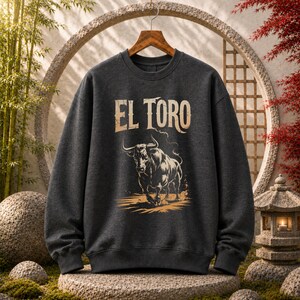 Peut inclure: Un sweat-shirt &agrave; col rond gris anthracite fonc&eacute; avec une impression graphique d'un taureau et le texte EL TORO &eacute;crit dans une police beige vieillie. Le motif repr&eacute;sente le taureau dans une posture de charge avec des ombres d&eacute;taill&eacute;es.