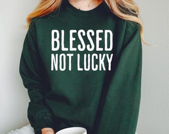 Puede incluir: Una sudadera verde oscuro con el texto "Blessed Not Lucky" en letras blancas.