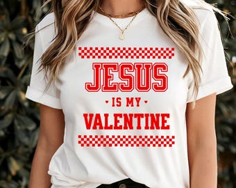 May include: White t-shirt with the text "JESUS IS MY VALENTINE" in red, with red checkered patterns above and below the text. The shirt is a casual style.