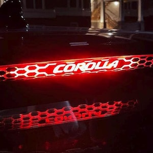 May include: A red and white car taillight with a honeycomb pattern and the word "COROLLA" in white letters.