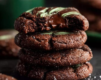 Puede incluir: Una pila de cuatro galletas de chocolate con un glaseado de chocolate y menta. Las galletas son de color marrón oscuro, espolvoreadas con azúcar gruesa y tienen un aspecto suave y texturizado. Una galleta tiene un mordisco, revelando el interior.