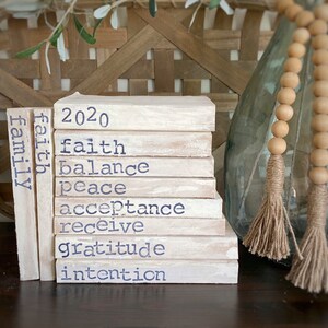 May include: A stack of white painted wooden blocks with the words "2020", "faith", "balance", "peace", "acceptance", "receive", "gratitude", "intention", and "family" written in blue paint.