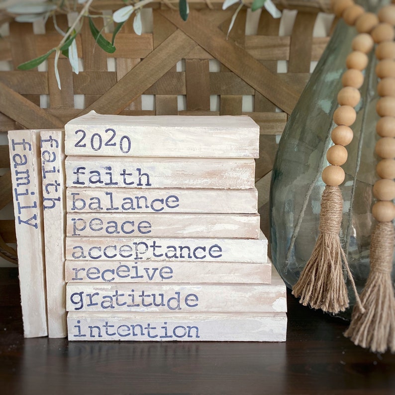 May include: A stack of white painted wooden blocks with the words "2020", "faith", "balance", "peace", "acceptance", "receive", "gratitude", "intention", and "family" written in blue paint.