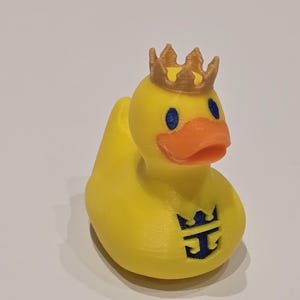 May include: A yellow rubber duck with a gold crown on its head and a blue and gold Royal Caribbean logo on its chest.