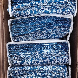 May include: Four stacks of blue and white patterned bed sheets are neatly folded and packaged in a cardboard box.